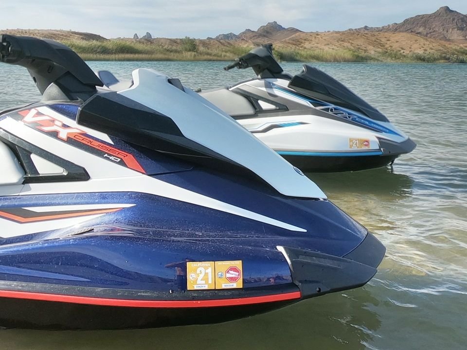 Two Yamaha WaveRunner personal watercraft floating on water with a desert mountain landscape in the background.