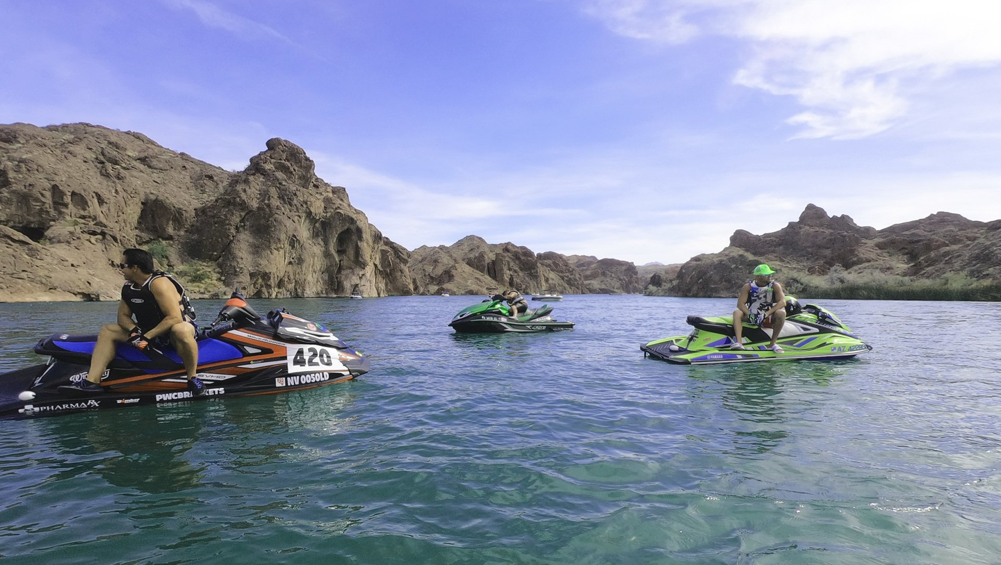 Riders on three jet skis on a lake below rocky hills