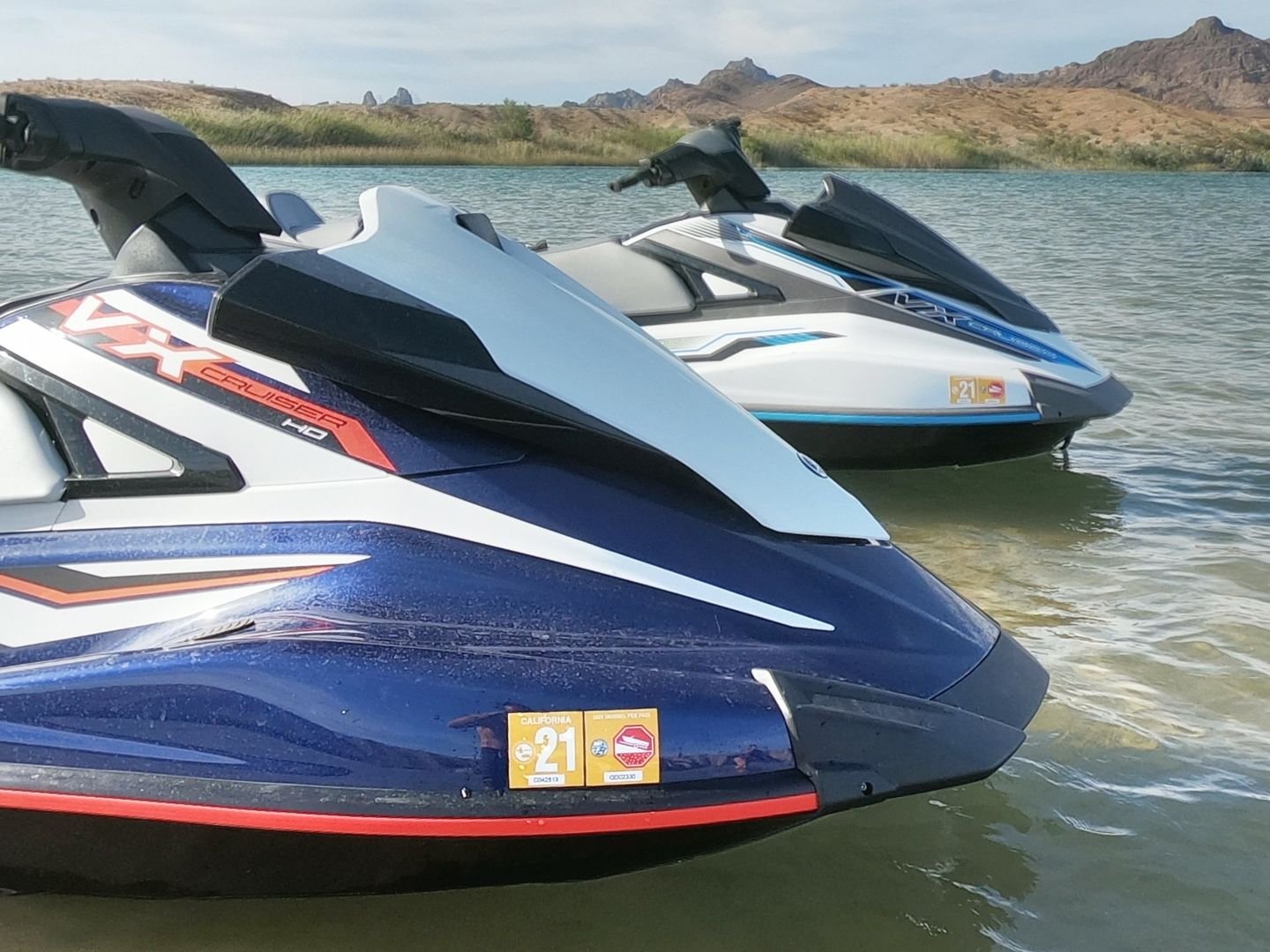 Two Yamaha WaveRunner personal watercraft floating on water with a desert mountain landscape in the background.