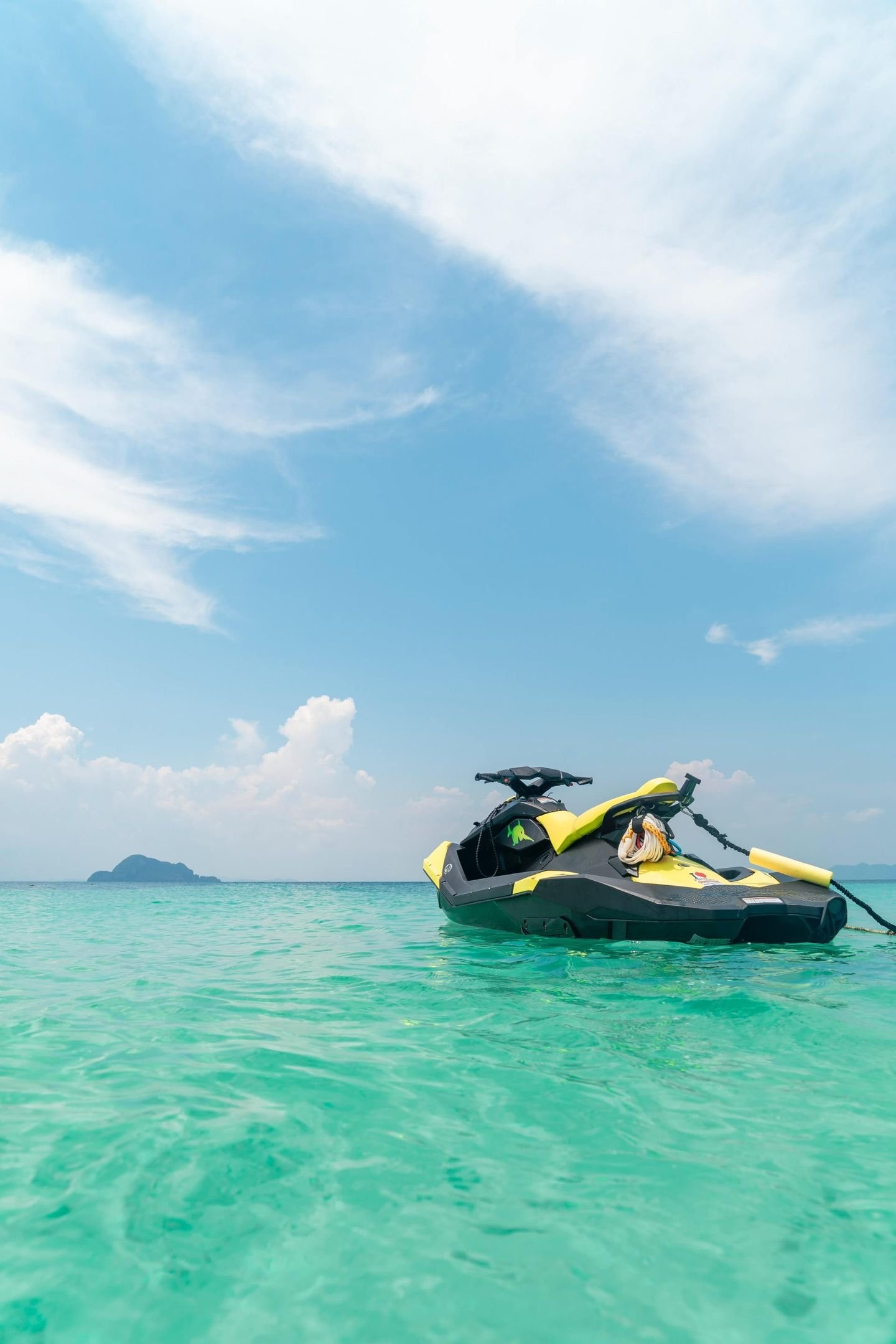 A bright yellow jet ski floats on clear, turquoise water under a blue sky with soft white clouds.